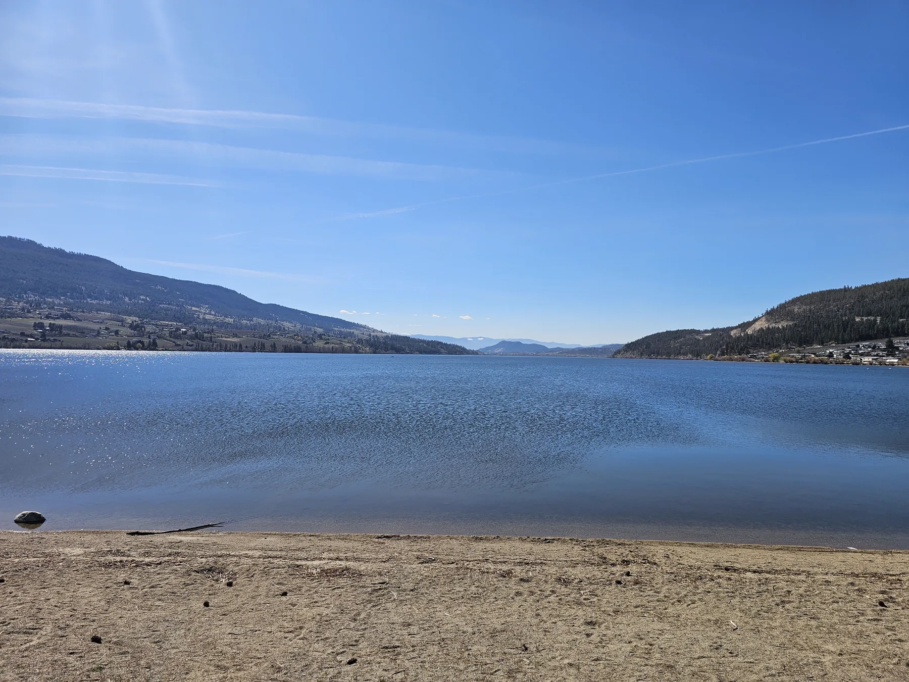 Wood Lake shoreline with calm water, a sandy beach and Okanagan hills under a blue sky